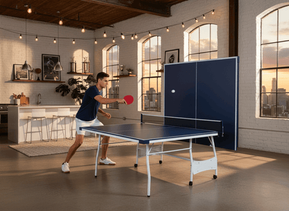 Person playing ping pong in a modern kitchen with large windows.