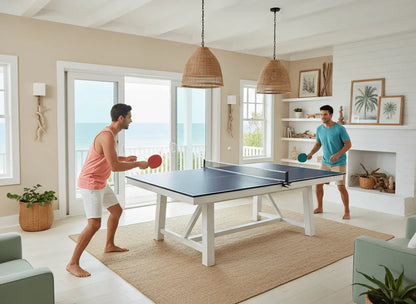 Two adults playing on a full-size ping pong table top in a bright coastal home game room
