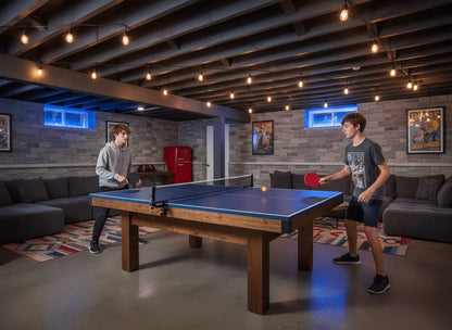 Two players using a blue ping pong table top installed on a pool table in a basement